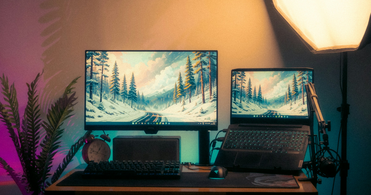 Monitor and laptop on a desk, both showing a winter road wallpaper.