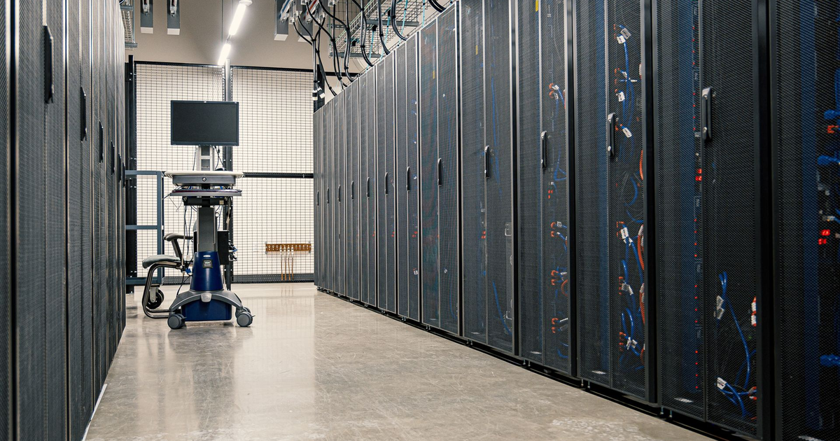 Aisle between rows of black server racks in a bright data center.